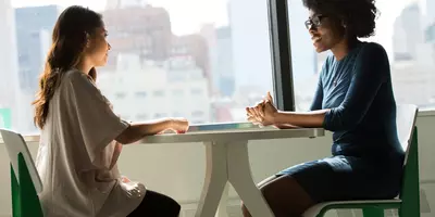 Zwei Frauen sitzen an einem Tisch und sprechen miteinander